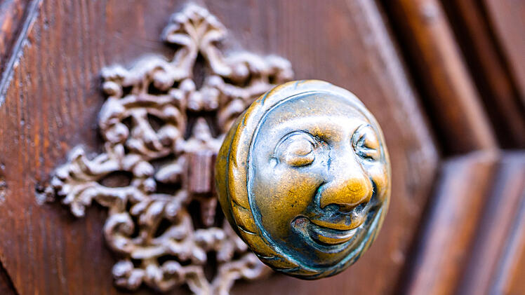 Ein kunstvoll geschnitzter T&uuml;rgriff mit einem l&auml;chelnden Gesicht, umgeben von einem dekorativen, floralen Muster, erinnert an die Spuren von E.T.A. Hoffmann in Bamberg.