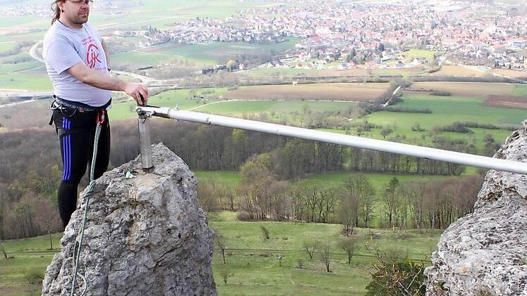 Markus Geiger aus Kronach steht, am Seil gesichert, auf dem schmalen Felsvorsprung und bringt den Fahnenmast in die Senkrechte.