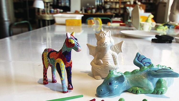 Keramikfiguren und Malpinsel auf einem Tisch laden zum Bemalen ein. Ein kreativer Ort für Kinderaktivitäten, passend zu familienfreundlichen Angeboten in Bamberg.
