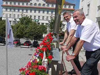 Zum Glück ist nicht alles so störrisch wie die Fahne zum Tag der Franken: Dr. Heiko Voigt (links) und Frank Rebhan blicken auf den Sonneberger Bahnhofsplatz, wo am Sonntag, 7. Juli, eine Festmeile startet. Foto: Berthold Köhler