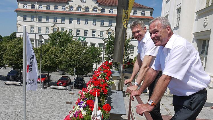 Zum Glück ist nicht alles so störrisch wie die Fahne zum Tag der Franken: Dr. Heiko Voigt (links) und Frank Rebhan blicken auf den Sonneberger Bahnhofsplatz, wo am Sonntag, 7. Juli, eine Festmeile startet. Foto: Berthold Köhler