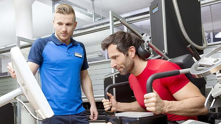 Ein Trainer zeigt einem Mann, wie ein Sport Gerät zu bedienen ist.