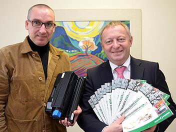 Andreas Sandwall (links) mit einer Tonerkartusche, die in Zukunft auch gesammelt und der Wiederverwertung zugeführt wird, und Landrat Thomas Bold mit den neuen Abfuhrkalendern. Foto: Peter Rauch