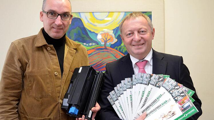 Andreas Sandwall (links) mit einer Tonerkartusche, die in Zukunft auch gesammelt und der Wiederverwertung zugeführt wird, und Landrat Thomas Bold mit den neuen Abfuhrkalendern. Foto: Peter Rauch