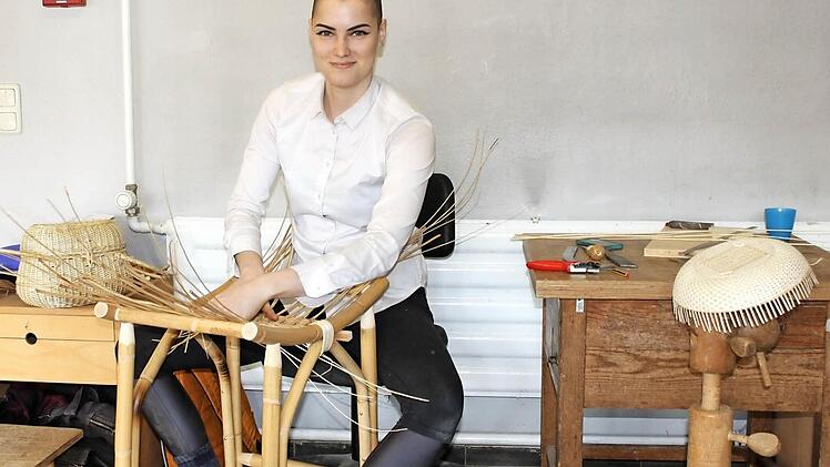 Gastschülerin Camille Labarre aus den Vereinigten Staaten ist wahrlich keine Anfängerin, was das Flechten angeht. Hier flicht sie die Sitzfläche eines Hockers aus. Die Handtasche links hinten im Bild hat sie während ihres Frankreich-Aufenthaltes geflochten, an der Schale aus feinen Weidenschienen rechts im Bild arbeitet sie noch. Foto: Popp