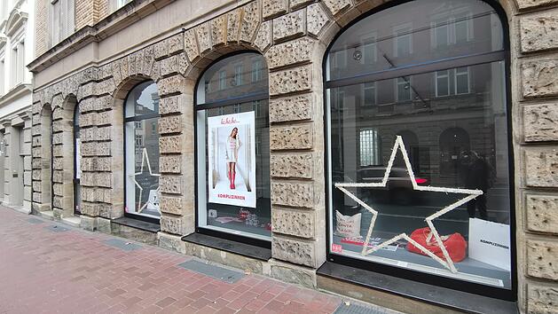 Ein Schaufenster in der Innenstadt mit gro&szlig;en Bogenfenstern zeigt weihnachtliche Dekoration wie beleuchtete Sterne und Plakate. Der Pop-up-Store bietet fair produzierte Produkte an.