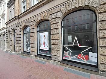 Ein Schaufenster in der Innenstadt mit großen Bogenfenstern zeigt weihnachtliche Dekoration wie beleuchtete Sterne und Plakate. Der Pop-up-Store bietet fair produzierte Produkte an.