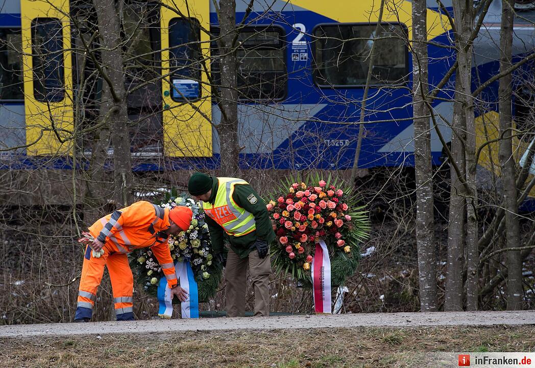 Ein Feuerwehrmann und ein Po lizist betrachten Kränze am 10.02.2016 vor der Unfallstelle eines Zugunglücks in der Nähe von Bad Aibling (Bayern) gerichtet. Bei dem Unglück waren mindestens zehn Menschen getötet worden, es gab rund 80 Verletzte. Foto: Sven Hoppe/dpa