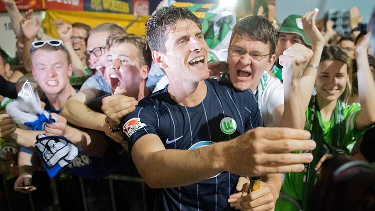Wolfsburgs Mario Gomez (M) feiert an einem Hinterausgang des Stadions mit den mitgereisten Fans den Klassenerhalt. Foto: Julian Stratenschulte/dpa