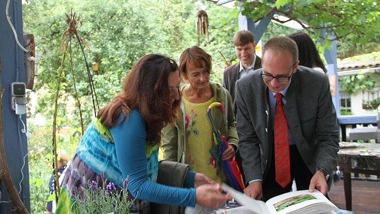 Burgkunstadts Bürgermeisterin Christine Frieß (Mitte), Kreisfachberater Michael Stromer (hinten) und Landrat Christian Meißner (rechts) betrachten das Garten-Gästebuch von Andrea Dembowski (links).