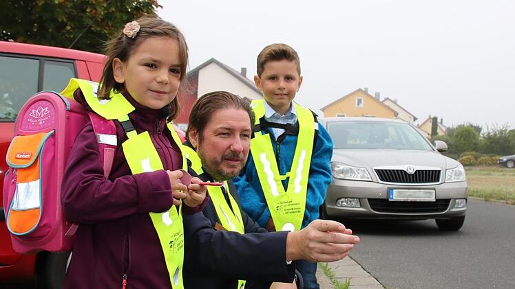 Verkehrserzieher Matthias Kleren erklärt zum Schulstart den beiden Abc-Schützen Leni und Timo das richtige Verhalten im Straßenverkehr. Ein Tipp: Nie zwischen parkenden Autos hindurch auf die Straße laufen.
