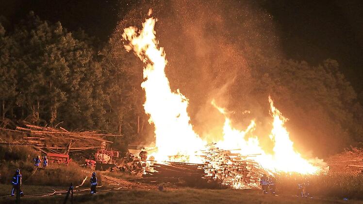Zahlreiche Feuerwehrleute wurden am späten Montagabend zum Brand eines Holzlagers gerufen. Nachdem das Feuer gelöscht war, riss ein Bagger den Holzhaufen auf, um weitere Glutnester sichtbar zu machen. Fotos: News5/Ferdinand Merzbach