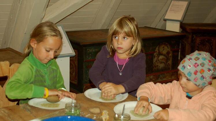 Mia, Stella und Lilith Buron zermalmen Kräuter mit einem Stein, um daraus Kräutersalz zu machen.