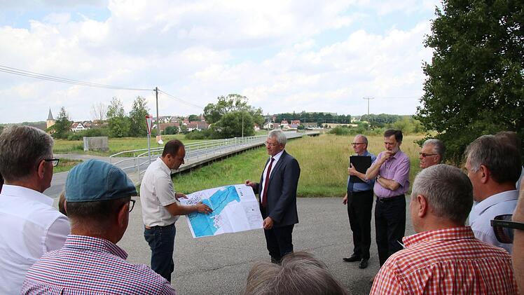 Mitten durch das Überschwemmungsgebiet zwischen den Pommersfeldener Ortsteilen Wind und Sambach (im Hintergrund) führt die BA 24, die samt Brücke über die Reiche Ebrach saniert wird. Ein Geh- und Radweg soll zusätzlich entstehen. Tiefbauer Michael Dotterweich (am Plan links) und sein Chef, Landrat Johann Kalb, erläuterten dem Bauausschuss vor Ort die Pläne.  Fotos: Sebastian Schanz