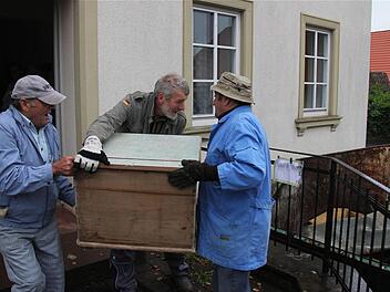 Helfer schleppen ein altes Möbelstück zum Container. Foto: Gerd Schaar