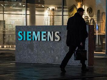 Ein Mann geht an dem Logo der Firma Siemens vorbei