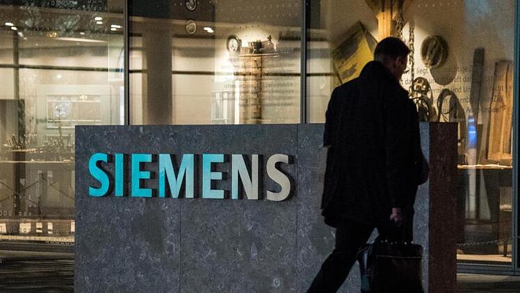 Ein Mann geht an dem Logo der Firma Siemens vorbei