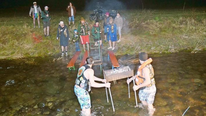 Der Grill wird vom Ufer in das kniehohe Wasser der Tettau getragen und verankert. Foto: Karl-Heinz Hofmann