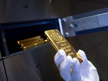 Mann legt einen Goldbarren in ein Schlie&szlig;fach eines Tresorraums