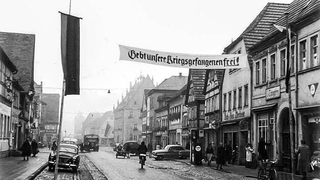 Dieses Bild zeigt die Ansicht der Oberen Hauptstra&szlig;e in Ha&szlig;furt um 1955. Bis zum Ende der 1960er Jahre sah es hier nicht wesentlich anders aus. Die Fahrbahn und die Parkstreifen wurden zwar auch noch asphaltiert, doch bei den Gesch&auml;ften blieb vieles erst einmal erhalten. Gut zu erkennen, die Zapfs&auml;ule der Firma Kirchner (rechts) Foto: Archiv Ludwig Leisentritt