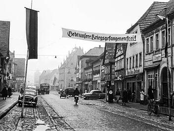 Dieses Bild zeigt die Ansicht der Oberen Hauptstraße in Haßfurt um 1955. Bis zum Ende der 1960er Jahre sah es hier nicht wesentlich anders aus. Die Fahrbahn und die Parkstreifen wurden zwar auch noch asphaltiert, doch bei den Geschäften blieb vieles erst einmal erhalten. Gut zu erkennen, die Zapfsäule der Firma Kirchner (rechts) Foto: Archiv Ludwig Leisentritt