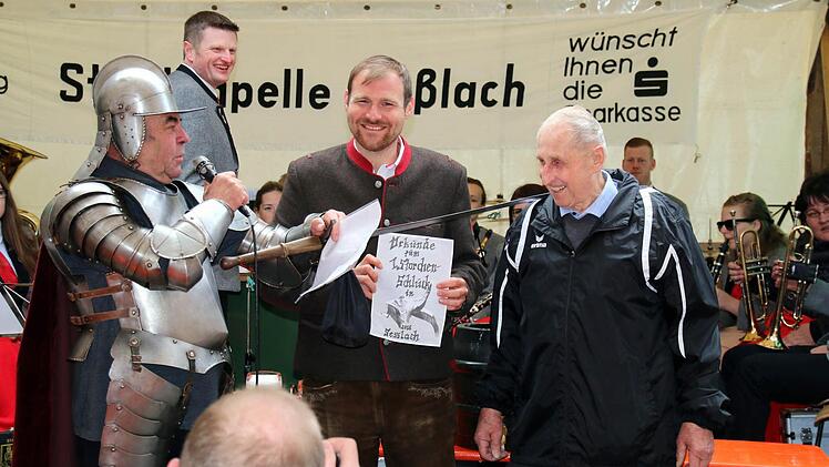 Mit dem Schwert und einer Urkunde zum 1. Storchenschluck adelten Ritter Heinrich zu Geiersberg (Heinz Winkelmann, links) und Bürgermeister Martin Mittag den Jubilar Alfred Gagel (rechts), der seit nunmehr 65 Jahren aktiv in der Stadtkapelle musiziert, sehr zur Freude von deren Leiter Michael Bauer (hinten). Foto: Bettina Knauth