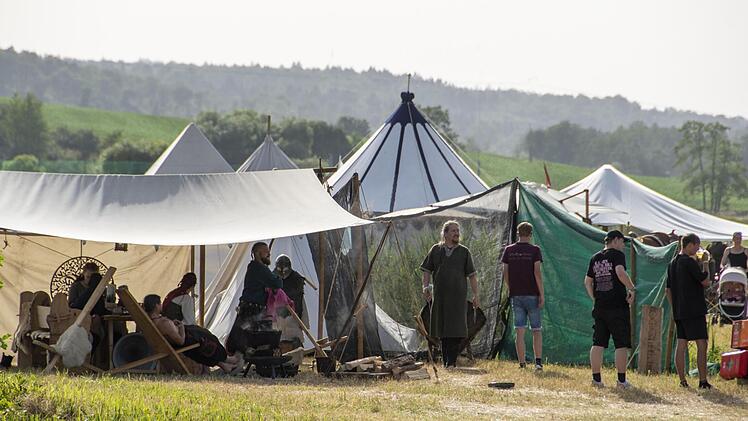 Zelte in Burgwindheim: Menschen in historischer Kleidung versammeln sich vor mittelalterlichen Zelten während eines sommerlichen Pilgerlagers, umgeben von malerischen Landschaften.