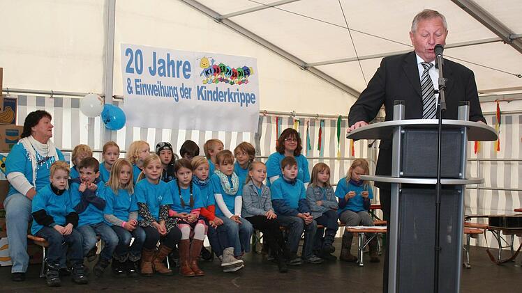 : Bürgermeister Waldemar Kleetz bei seiner Rede. Im Hintergrund warten die Hortkinder auf ihren musikalischen Einsatz