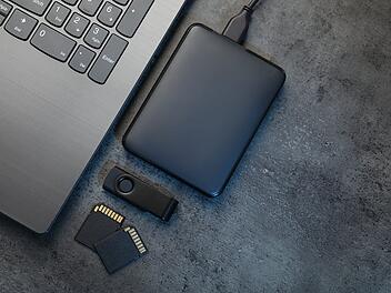 SD memory cards, USB flash drive, hard disk drive with cable and laptop on dark grey table, flat lay. Space for text SD-Speicherkarten, USB-Stick, Festplatte mit Kabel und Laptop auf dunkelgrauem Tisch, flach liegend. Platz für Text