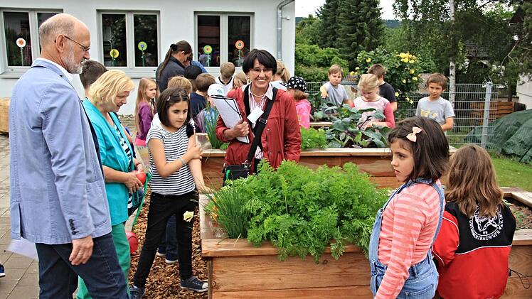 Zweiter Bürgermeister Siegfried Kirchner (links) erklärt Elfriede Weikard (vorne Vierter von links) von der Bewertungskommission die Hochbeete der Kinder an der Grundschule.