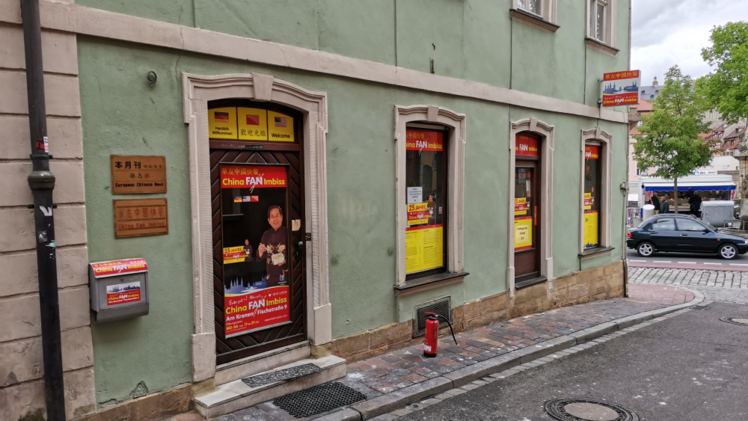 Ein Bamberger China-Imbiss hat eine Aktion zur Zeugnisvergabe gestartet. Das Gebäude ist grün mit Plakaten, die Angebote und die Adresse darstellen. Schüler profitieren unabhängig von den Noten.