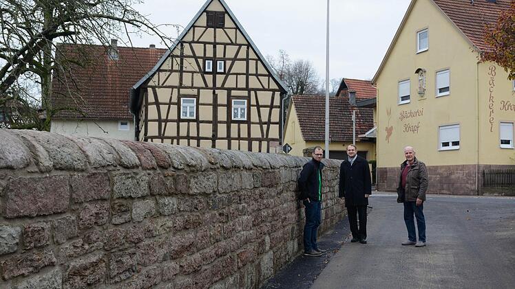 Sind froh darüber, dass die Mauer am Aschacher Kindergarten nicht abgerissen wurde (von links): Andreas Brehm (Rechnungsführer der Kirchenstiftung), Pfarrer Michael Kubatko und Kirchenpfleger Walter Hein. Foto: Björn Hein