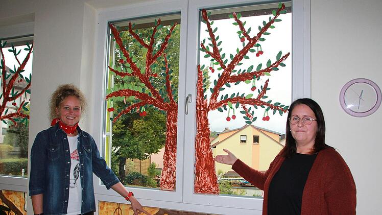 Die Erzieherinnen Nicole Kleinhenz (l.) und Susanne Metz  zeigen auf einen gemalten Baum. Die Wurzeln stehen als Symbol f&uuml;r das Urvertrauen des Kindes, das es braucht, damit es den Herausforderungen des Lebens standhalten kann. Foto: Wittnebel-Schmitz