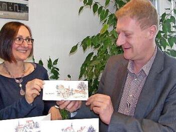 Die von ihr gestalteten Karten zeigt Künstlerin Silvia Huber im Sonnefelder Rathaus Bürgermeister Michael Keilich. Sie hat für Sonnefeld, Hassenberg und Gestungshausen Motivvariationen angefertigt.  Foto: K. Oelzner