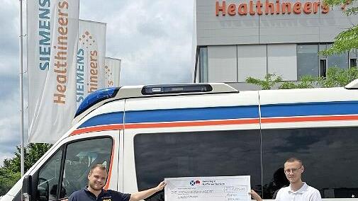 Der ehemalige Azubi bei Siemens Healthineers, Lucas Spörl (rechts), übergibt Lukas Hänsch vom ASB-Wünschewagen einen Scheck über 1600 Euro.