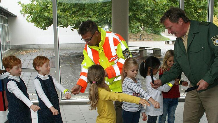 Die Haßfurter Erstklässler waren mit die ersten, die von der Kreisverkehrswacht mit reflektierenden Klickbändern ausgestattet wurden. Da traten die Buben und Mädchen gerne an, um sich von Stefan Scherrer (links) und Dominique Heim die Geschenke direkt an die Handgelenke legen zu lassen. Foto: Sabine Weinbeer