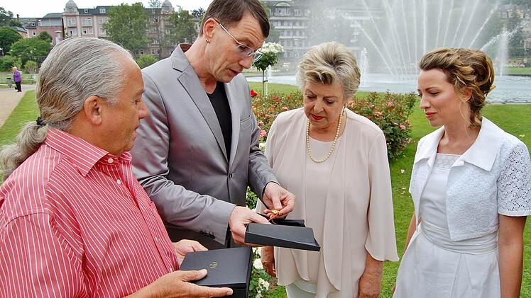 Schmuckdesigner Malte Meinck (Zweiter von links) beschenkt Bad Kissingens Botschafterinnen, die Schauspielerinnen Marie-Luise Marjan (Mitte) und Sanny van Heteren, mit einem von Porzellanmaler Ehrenfried Riegel (links) gemalten Rosen-Anhänger aus Porzellan.