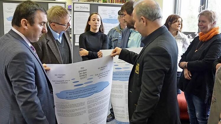 Imam Niyazi Cabbar und Ramazan Kurt halten eines der Plakate für die Ausstellung "Gebete im Dialog". Dahinter Religionslehrerin Nina Rossa, die die interreligiösen Gebete mit Schülern des Arnold-Gymnasiums erarbeitet hat. Foto: Rainer Lutz