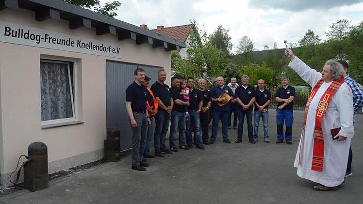 Voller Stolz ist die Vorstandschaft der Bulldogfreunde Knellendorf auf ihr neues Vereinsheim, welchem Pater Waldemar Brysch mit einem Segensgebet und durch Besprengen mit Weihwasser die Weihe erteilt. Foto: Karl- Heinz Hofmann