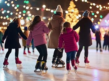 Families and friends enjoying ice skating during a festive evening at a busy outdoor rink surrounded by twinkling lights and a Christmas tree