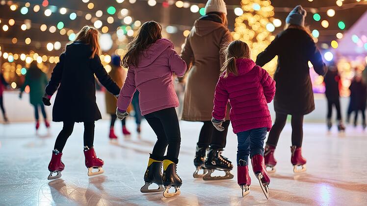 Families and friends enjoying ice skating during a festive evening at a busy outdoor rink surrounded by twinkling lights and a Christmas tree