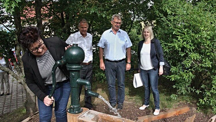 "Spieldrang" auch bei der Chefin des Kindergartens, Dagmar Klee, die kräftig den Pumpschwengel bedient und das Wasser sprudeln lässt. Hinten beobachten das (von links), Firmenchef Stephan Rösler, Bürgermeister Helmut Dietz und die Leiterin der Kommunikation der Firma Rösler, Julia Lips. Foto: Helmut Will