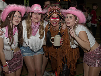 Menschen feiern auf einer Faschingsveranstaltung in Franken. Sie tragen fröhliche Kostüme, darunter Cowboyhüte und ein indianisches Outfit, und posieren lächelnd für die Kamera.