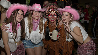 Menschen feiern auf einer Faschingsveranstaltung in Franken. Sie tragen fröhliche Kostüme, darunter Cowboyhüte und ein indianisches Outfit, und posieren lächelnd für die Kamera.