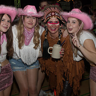 Menschen feiern auf einer Faschingsveranstaltung in Franken. Sie tragen fröhliche Kostüme, darunter Cowboyhüte und ein indianisches Outfit, und posieren lächelnd für die Kamera.