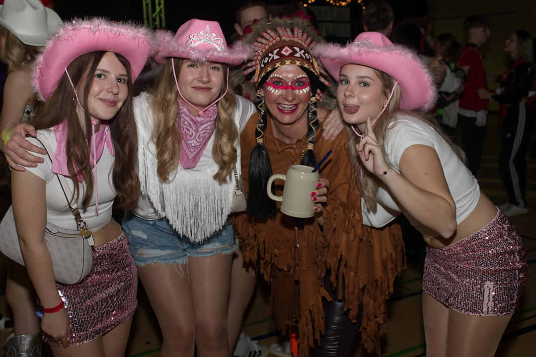 Menschen feiern auf einer Faschingsveranstaltung in Franken. Sie tragen fröhliche Kostüme, darunter Cowboyhüte und ein indianisches Outfit, und posieren lächelnd für die Kamera.
