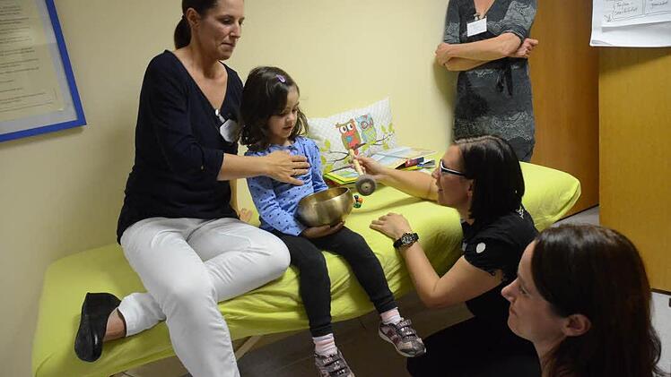 Die vierjährige Johanna genießt beim Babytag das Auflegen der Hände von Osteopathin Anja Möckel (links) und die sanften Töne der Klangschalen von Heilpraktikerin Lisa Felsecker (Zweite von rechts). Foto: Karl-Heinz Hofmann