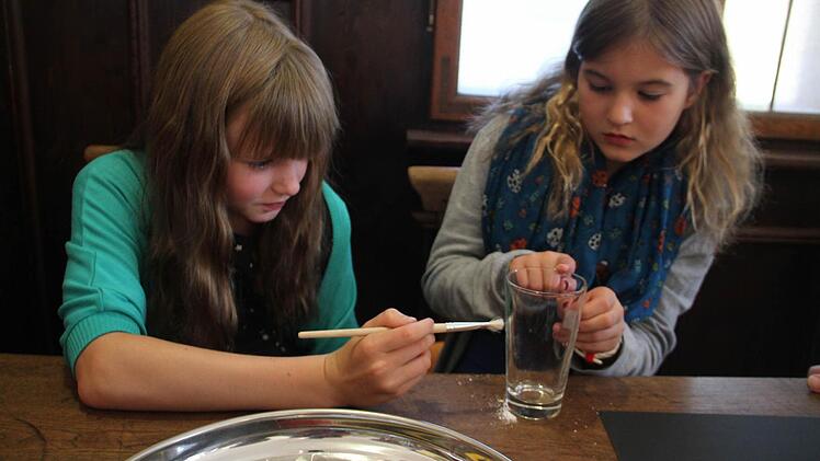 Jule (links) und Marit (rechts) nehmen einen Fingerabdruck von einem Wasserglas.