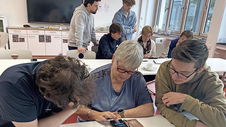 Zwei Sch&uuml;ler unterst&uuml;tzen eine Seniorin bei der Einstellung der Standortfreigabe auf ihrem Smartphone.
