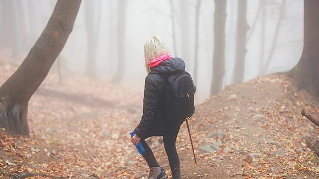 Eine geheimnisvolle Frau wandert allein auf einem Waldweg, umh&uuml;llt von dichtem Nebel, der eine unheimliche und mystische Atmosph&auml;re schafft. A mysterious woman walks alone on a forest trail, enveloped by thick fog, creating an eerie and mystical atmosphere